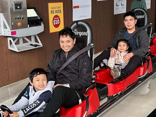 A family of four sits on a ride, smiling and enjoying their time together at an amusement park.