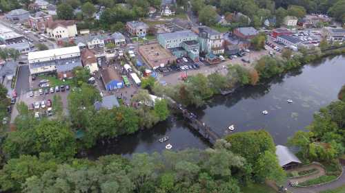 Aerial view of a riverside town with buildings, trees, and people enjoying activities along the water.