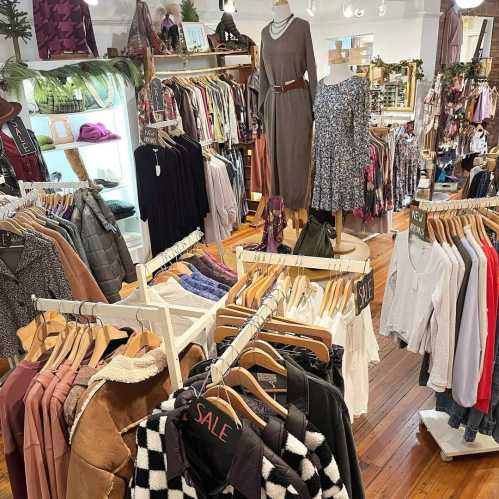 A clothing store interior featuring racks of various garments, including dresses, tops, and jackets, with a "SALE" sign.