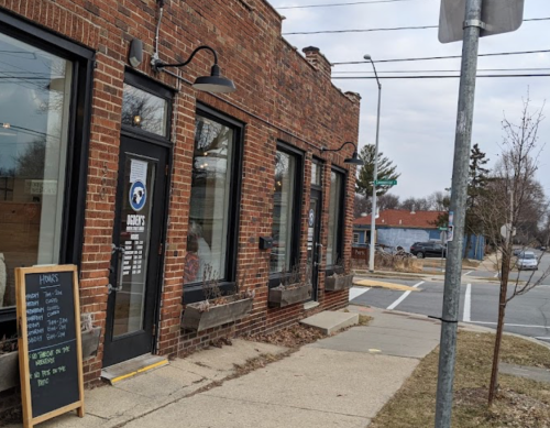 A brick building with large windows, planters, and a sign for a business, located on a sidewalk near a street corner.