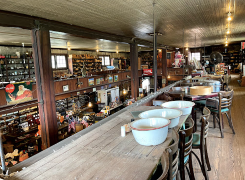 A vintage store interior with wooden beams, shelves filled with antiques, and a view from a second-floor balcony.