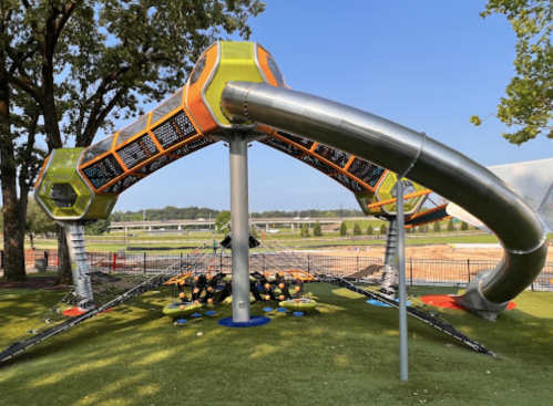 A colorful playground structure with slides and climbing features, set on green grass under a clear blue sky.