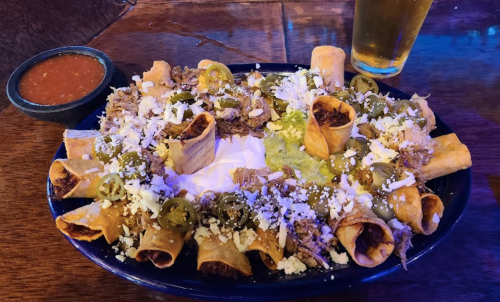 A plate of loaded nachos topped with jalapeños, cheese, guacamole, sour cream, and a side of salsa, with a beer nearby.