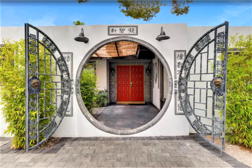 A circular gate opens to a pathway leading to red doors, framed by bamboo and decorative walls.