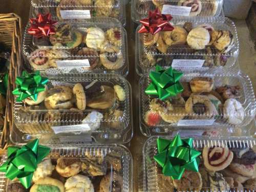 A display of assorted cookies in clear containers, each topped with festive red and green bows.