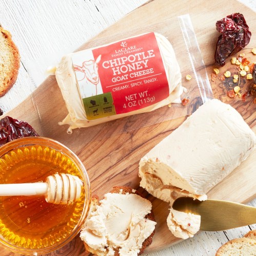 A wooden board with chipotle honey goat cheese, honey, and crackers, showcasing a creamy, tangy spread.