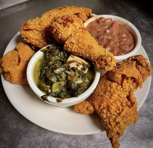 A plate of crispy fried chicken with sides of collard greens and red beans.