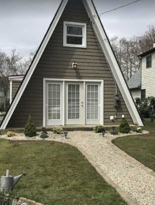 A-frame house with a brown shingle exterior, double doors, and a landscaped front yard with gravel and small plants.