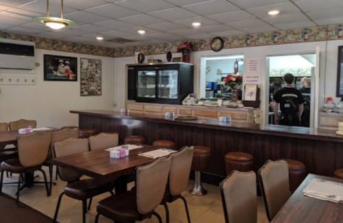 A cozy diner interior with wooden tables, chairs, and a counter, featuring a kitchen area in the background.