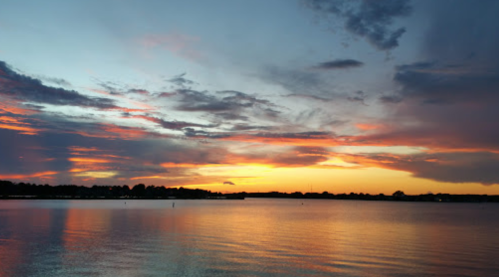 A serene sunset over a calm lake, with vibrant orange and purple hues reflecting on the water.