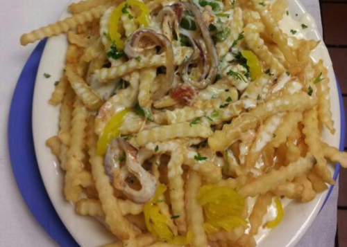 A plate of crinkle-cut fries topped with sauce, sliced onions, and yellow peppers, garnished with parsley.