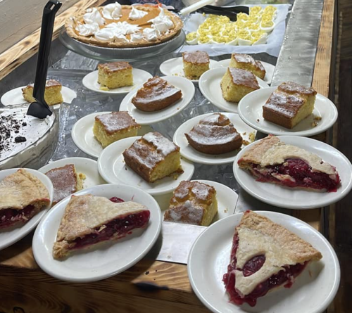 A variety of desserts on plates, including pie slices and cake, displayed on a wooden table.