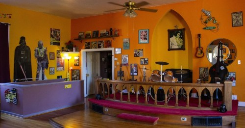 A vibrant room with a stage, drum set, guitars, and eclectic wall art, featuring a Darth Vader mural.
