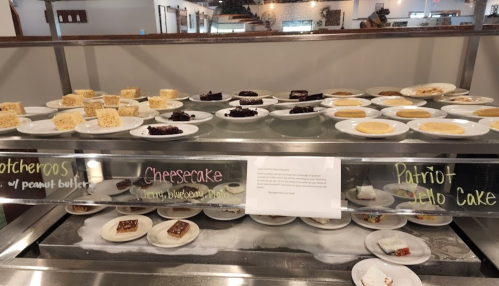 A dessert display featuring various cakes and treats, including cheesecake and peanut butter bars, on white plates.