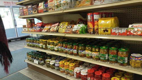 A grocery store shelf filled with various snacks, canned goods, and packaged foods in organized rows.