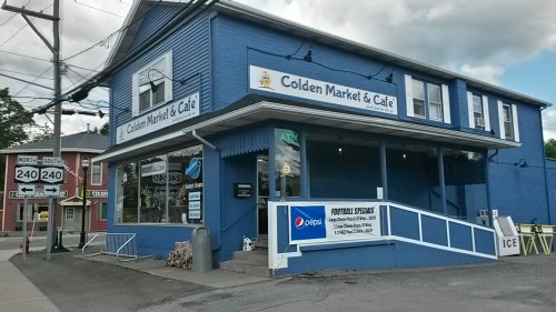 A blue building with a sign reading "Golden Market & Café," featuring an ATM and Pepsi advertisement outside.