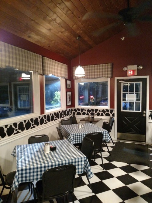 Cozy restaurant interior with checkered tables, cow-patterned walls, and large windows, featuring a warm, inviting atmosphere.