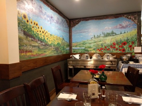 Cozy restaurant interior with vibrant mural of sunflowers and poppies, wooden tables, and a buffet setup.
