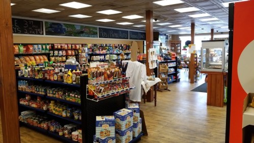 A well-stocked store interior featuring shelves of snacks, groceries, and household items, with wooden accents.
