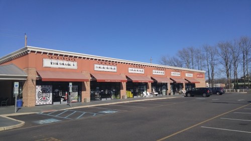 A row of storefronts with awnings, featuring "The Shack" and other businesses, under a clear blue sky.