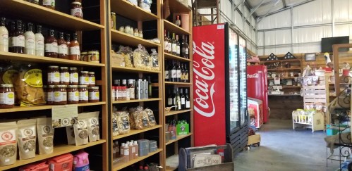 A cozy store interior featuring shelves of various products, including sauces, snacks, and a Coca-Cola vending machine.