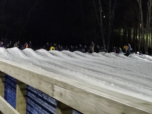 A snowy hill with people tubing in the background, illuminated by lights at night.