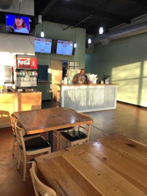 A bright, modern café interior with wooden tables, a counter, and a staff member preparing orders.