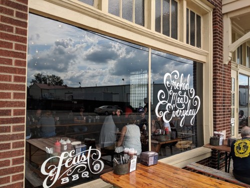 A BBQ restaurant with a large window displaying the words "Smoked Meat Everyday," and diners visible inside.