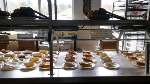 A display of various desserts on plates, including cakes and pies, in a bakery setting.