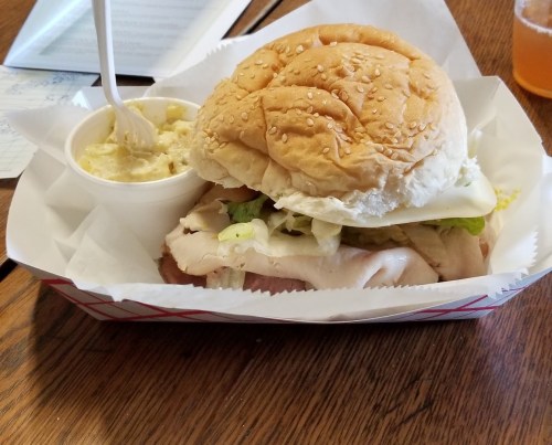 A sesame seed bun sandwich filled with turkey, lettuce, and cheese, served with a side of creamy soup in a cup.