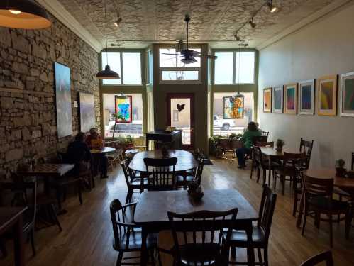 Cozy café interior with wooden tables, stone walls, and colorful artwork, featuring patrons enjoying their time.