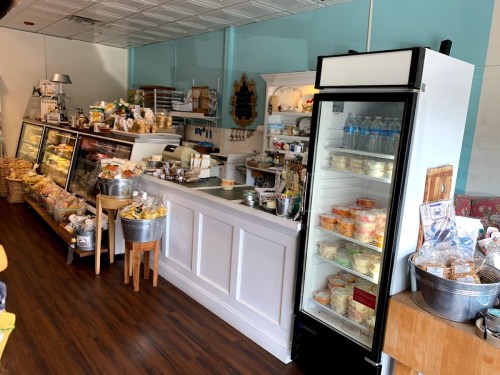 A cozy café interior featuring display cases of baked goods, a drink fridge, and a wooden seating area.