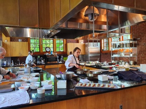 A busy kitchen with chefs preparing dishes, featuring stainless steel appliances and a variety of ingredients on the counter.