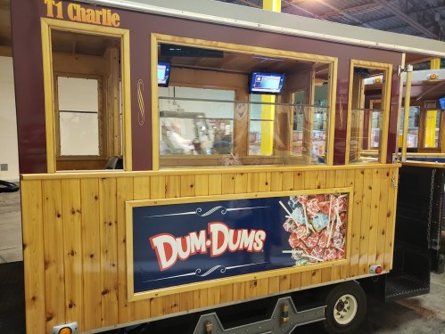 A wooden cart with a sign reading "DUM-DUMS," featuring two screens inside and a cozy, rustic design.