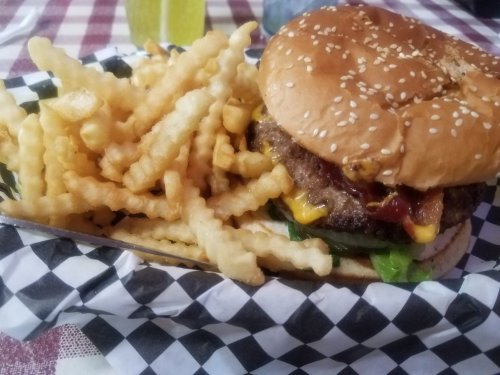 A sesame seed burger with lettuce, cheese, ketchup, and fries in a checkered basket on a table.