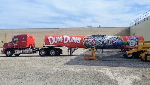 A colorful truck trailer featuring a large advertisement for Dum-Dum lollipops parked in a lot.