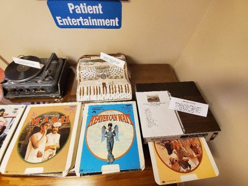 A table displaying vintage records, a record player, and an accordion under a sign reading "Patient Entertainment."
