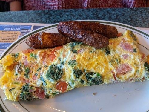 A plate featuring a colorful vegetable omelette with ham and two sausage links on the side.