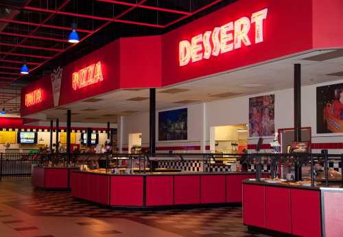 A brightly lit buffet area featuring pizza and dessert stations with red decor and checkered accents.