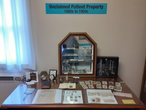 Display of unclaimed patient property from the 1880s to 1950s, featuring various personal items and documents.