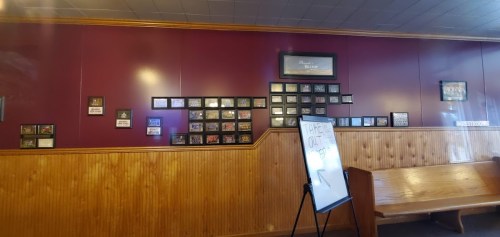 A restaurant wall featuring framed photos and plaques, with a whiteboard in front displaying a message.