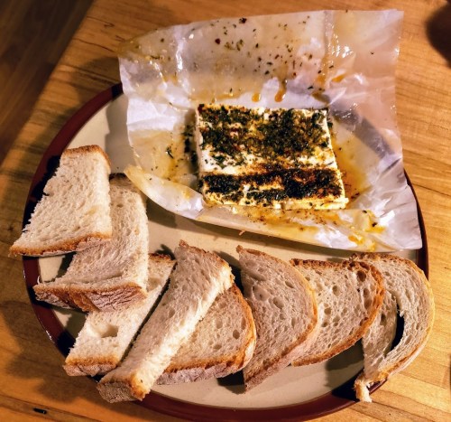 A plate with slices of bread and a piece of baked tofu topped with herbs and spices on parchment paper.