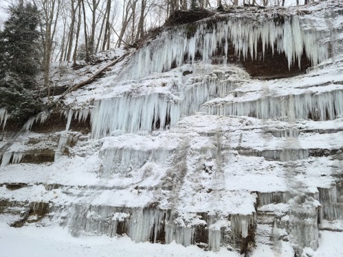 A snowy cliffside adorned with large icicles hanging from layered rock formations.