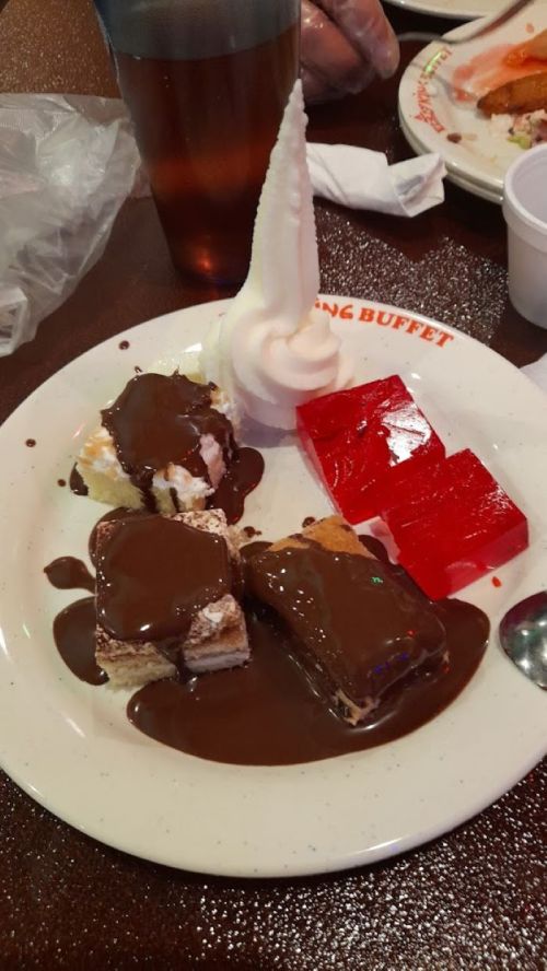 A plate with chocolate-drizzled desserts, including cake, ice cream, and red gelatin, served at a buffet.