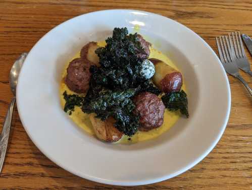 A plate of meatballs with crispy kale, roasted potatoes, and a creamy sauce, served on a wooden table.