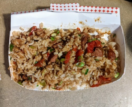 A takeout container filled with fried rice, diced vegetables, and pieces of meat.