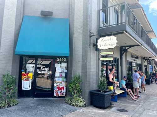 Exterior of a café named "Sweet Nothings," with a blue awning and people sitting outside on a sunny day.