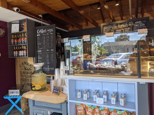 A cozy café interior featuring a coffee menu, display case with pastries, and a lemonade jar on a wooden counter.