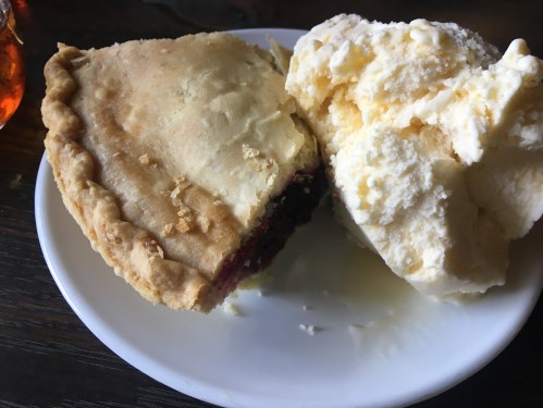 A slice of pie with a flaky crust next to a scoop of creamy vanilla ice cream on a white plate.