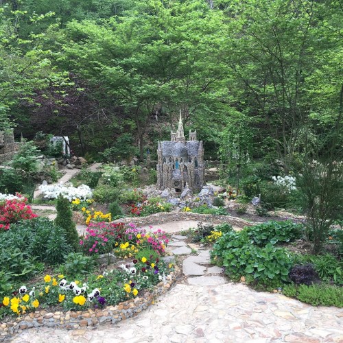 A lush garden with colorful flowers, stone pathways, and a whimsical castle-like structure surrounded by greenery.